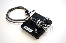 A commercially manufactured iambic paddle used in conjunction with an electronic keyer to generate Morse code. The sequence of dits and dahs is determined by the operator, but their timing is controlled by the separate keyer that the paddle key plugs into. Bencher paddle.jpg