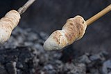 Bread dough rolled into a snake and wrapped helically around a stick, being browned over a fire like a marshmallow