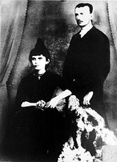 photographie noir et blanc : un couple ; la femme est assise, l'homme debout à droite