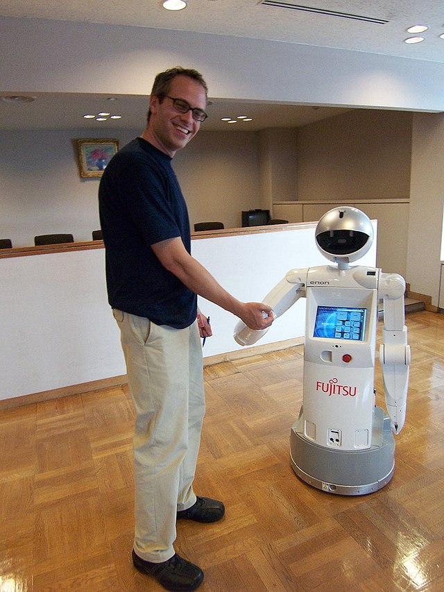 A man is shaking hands with a small humanoid robot