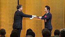 Araki (right) receiving an Art Encouragement Prize from Masahiko Shibayama, 2019