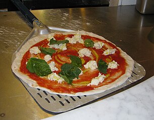 An unbaked Neapolitan pizza on a metal peel, ready for the oven