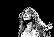 A black and white photograph showing a headshot of Robert Plant with a microphone in hand