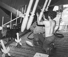 Rockets are loaded onto the folded wing of a TBM-3 Avenger of Composite Squadron 96 on the flight deck of Shamrock Bay in preparation for strikes to be conducted in support of the Battle of Okinawa. Note the extended Yagi-Uda antenna visible on the left side of the photo.