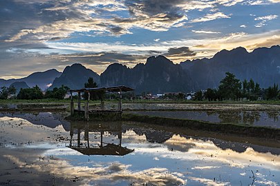 Water reflection of a wooden hut with colorful sky and karst mountains in a paddy field at sunset Vang Vieng Laos.jpg