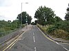 A single track road rises to pass over a bridge. A traffic light controls the traffic flow