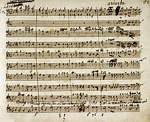 Reprodukce ruční partitury, čtyři takty a deset notových linek pod sebou; nažloutlý papír