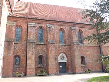 Nördliches Seitenschiff, Fas­sade zwei­geschos­sig und Fenster­formen wie Südseite, gotisches Portal mit ersetz­tem char­riertem Tympanon