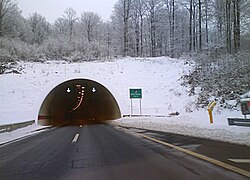Tunnel portal in a snow covered slope, variable traffic signs indicating traffic flow direction are visible at the tunnel entrance