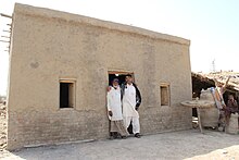 Two Sindhi men, one wearing Godd and Sindhi traditional floral rumal (handkerchief) as turban. A newly built, flood-resistant house in Pakistan's Sindh province.jpg