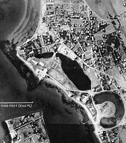 Una fotografía aérea en blanco y negro de un área urbana junto al mar con una entrada en forma de toro llena de agua.