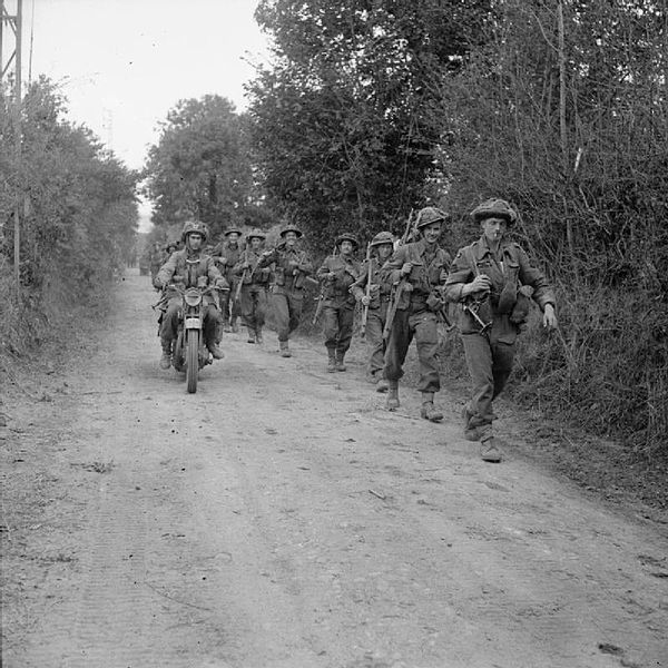 A motorcycle and infantry of the 2nd Battalion, Glasgow Highlanders, 46th Infantry Brigade, 15th (Scottish) Infantry Division, advance along a lane ne