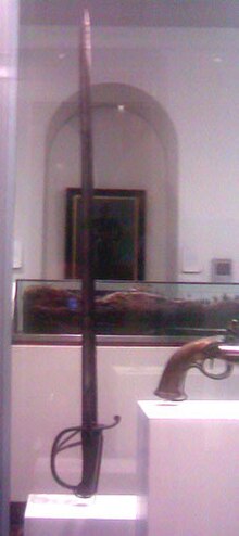 A sword is arranged in a glass case in a museum next to other antique weapons