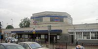 A light grey building with a long, rectangular, dark blue sign reading "HOUNSLOW WEST STATION" in white letters all under a cloudy sky