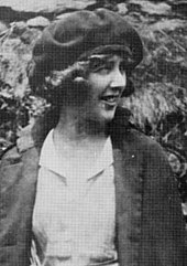 photographie de qualité médiocre d'une jeune femme en manteau, chemisier, coiffée d'un chapeau rond mou