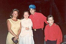 Een lachende Jackson draagt ​​een blauwe baseballpet en een rood shirt.  Rechts van hem staan ​​twee vrouwen.  De ene houdt een pen vast en de ander een kleine portemonnee.  Links van hem kijkt een jonge jongen buiten beeld.  Hij is ook gekleed in een rood shirt.  Jacksons hand ligt op zijn schouder.