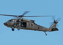 A gray-black helicopter flies against a clear blue sky, with some motion blur on the rotors.