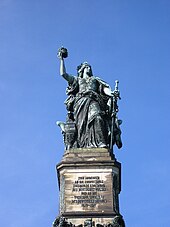 allegorical figure of Germania (woman with flowing robes, sword, flowing hair) standing, holding crown in right hand, sword partially sheathed