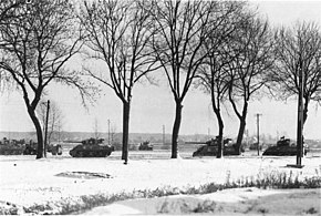 Fotografía en blanco y negro de una columna de tanques en la nieve, detrás de los árboles