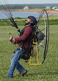Paramotor pilot "reverse launching", showing how seat bottom moves to allow for easy ground handling Wiki Paramotor by JeffGoin At PEI.jpg
