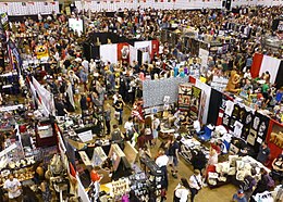 Photograph of the Expo in progress, taken from a high vantage point, showing crowds of attendees among booths arranged in a grid.