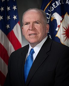 shoulder high portrait of man in his fifties or sixties standing in front of an American flag and the flag of the CIA