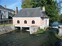 Farvefoto af en bygning, hvis facade viser skiftende senge af sten og mursten bygget over en strøm.