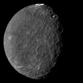 A round spherical body with its left half illuminated. The surface is dark and has a low contrast. There are only a few bright patches. The terminator is slightly to the right from the center and runs from the top to bottom. A large crater with a bright ring on its floor can be seen at the top of the image near the terminator. A pair of large craters with bright central peaks can be seen along the terminator in the upper part of the body. The illuminated surface is covered by a large number of craters.