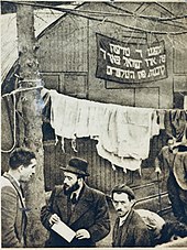 Rabbi Shlomo Zev Zweigenhaft (center with hat) speaking to Captain Ike Aronowicz of the Exodus (left) outside a Nissen hut during a visit to a DP camp in Poppendorf Poppendorf.jpg