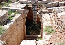 Un pasillo construido con sillares conduce a un arco en ruinas.