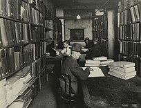 Black-and-white photo of men reading braille books in a small room packed with bookshelves