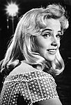 Close-up hitam-dan-putih foto potret tersenyum wanita muda dengan rambut pirang panjang di sebuah studio, cerah diterangi oleh lampu