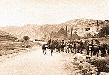 Mounted troopers in the foreground and another group in the middle distance on a road winding between high hills