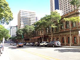 vista da Ann Street ao sol com alguns carros em movimento, carros estacionados em frente à estação ferroviária central