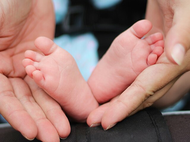 Mother's hands frame baby's feet (Image via Wikimedia Commons)