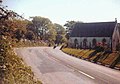 TT rider Mick Grant just after the crossroads passing the chapel on his descent of the hill during the Formula 1 TT in 1985[original research?]