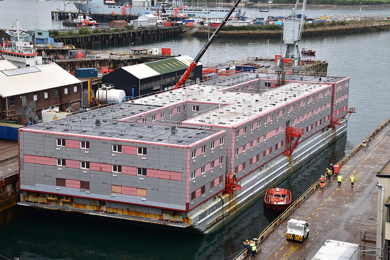 A red and grey, box-shaped hotel barge. It is four storeys tall and looks like an office block or similar high-density building.