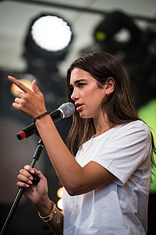 List Of Awards And Nominations Received By Dua Lipa Wikipedia - dua lipa performing in a white shirt with a microphone and her left hand pointing