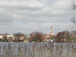 Ein See mit Schilf am Küstenvorland und eine Stadt am anderen Ufer