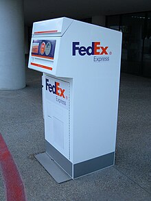 Fotografía en color de un quiosco de contenedores FedEx blanco.