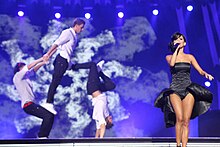 A photograph of Inna performing in a black dress while accompanied by three male backup dancers.