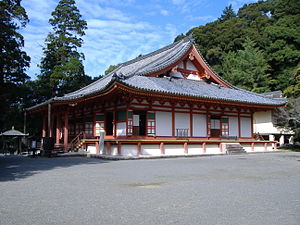 Wooden building with raised floor, white walls, vermillion red beams, an open veranda and a hip-and-gable roof.