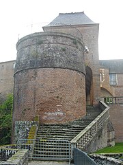 Photo couleur d'une courtine terminée par une tour de même niveau. Une autre tour en brique rouge couronnée d'un belvédère à garde-corps en fer forgé est contournée par un escalier qui mène des terrasses à la promenade et au jardin. Au-dessus, dépasse le toit en ardoise de l'aile dite de Stainville.