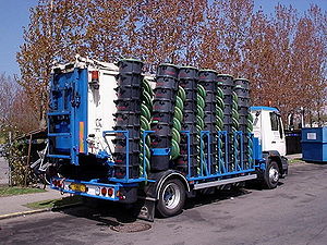 A truck similar in style to a garbage truck totes approximately 40 bins of food collected from a number of large kitchens. If the truck is associated with a company, the logo is not visible.