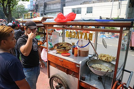 The street vendor is deep frying batagor in cart during car free day in Jakarta.