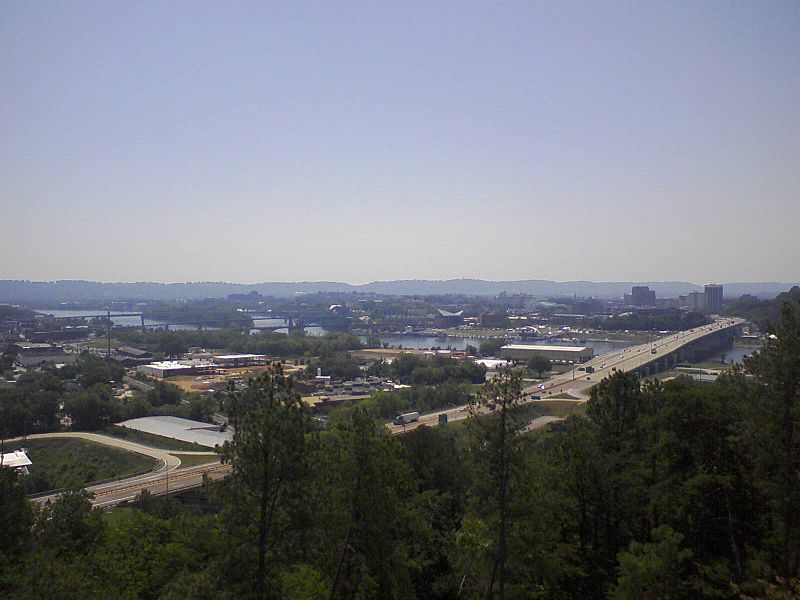  A view of Chattanooga from the north side of the Tennessee River.  The Tennessee Aquarium is the two buildings in the middle of the opposite side of the river, with the pointed roofs.  The sun is gleaming off the saltwater aquarium, on the left.  The four bridges of Chattanooga are pictured.  From right to left: The Olgiati Bridge, Market Street Bridge, Walnut Street Bridge, and Veteran's Bridge.  Missionary Ridge is in the far background.