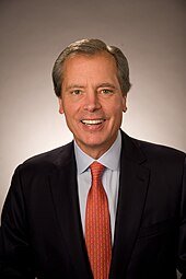 Headshot of a middle aged man in a suit with brown hair and hazel eyes.