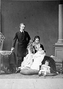 debout et revêtu d'une redingote sombre, le duc se tient aux côtés de sa fille aînée vêtue de clair et à la coiffure opulente de la duchesse assise portant sur les genoux sa fille nouvelle-née et aux pieds de laquelle Élisabeth est assise sur un coussin