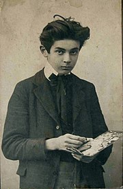 Černobílý americký snímek vážně vypadajícího dospívajícího chlapce v tmavém obleku, paleta v ruce