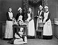 Elever vid Uppsala Hushållsskola. Flickorna är klädda i mörka klänningar och ljusa förkläden - Nordiska Museet - NMA.0034063.jpg